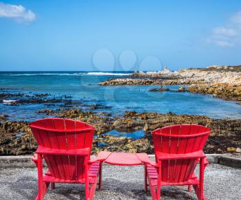 Two red armchairs chaise longue by Atlantic ocean. Boulders Penguin Colony in the Table Mountain National Park, South Africa. The concept of ecotourism
