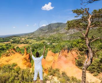  The elderly woman performs yoga in special form. Orange and red picturesque hills in Roussillon