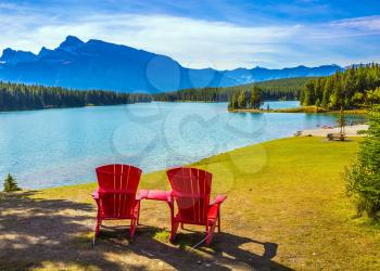 The morning sun warms the picturesque lake Two Jack. On the beach there are red chaise lounges.   The concept of ecological and active tourism
