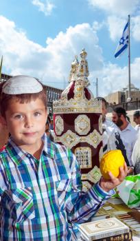 The Jews brought the Torah Scroll for prayer. Beautiful Jewish boy in white skullcap, with etrog. Jewish holiday Sukkot