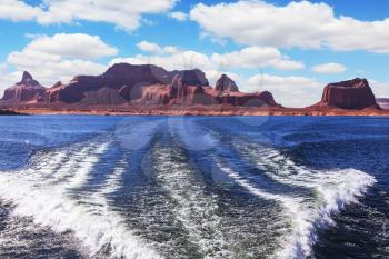  Foamy trace of a motor boat crosses the emerald waters. In distance the coast of red sandstone. Lake Powell on the Colorado River