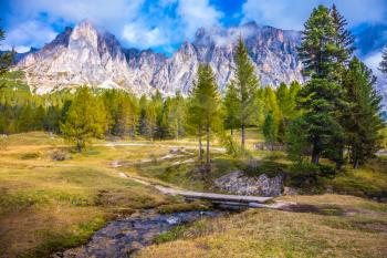  The concept of ecological and extreme tourism. Sharp rocks surround the grassy valleys. A cold fast spring flows through the valley. The dizzying Dolomites