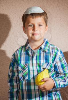 The charming seven-year-old boy in a white festive skullcap holds citrus in hand. The etrog - ritual fruit for the Jewish holiday of Sukkot