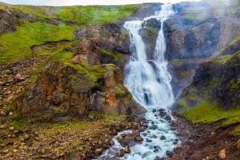 Concept of active and extreme tourism. Powerful streams of cascade falls with a roar break against cold rocks. Cold and rainy July in Iceland