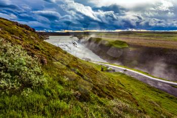 Windy and cloudy summer day. On the shore of the waterfall is a path for tourists. Incredible Golden Falls - Gulfoss in Iceland. The concept of extreme and phototourism