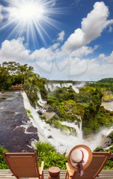 Scenic basaltic rock formations famous waterfalls Iguazu Falls. The concept of ecological tourism. Two wooden chaise longue stand near the waterfalls