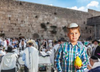 People in white Taliths pray at the Western Wall of the Temple - the greatest shrine of Judaism. Autumn Jewish holiday Sukkot. Beautiful Jewish boy in white skullcap, with etrog
