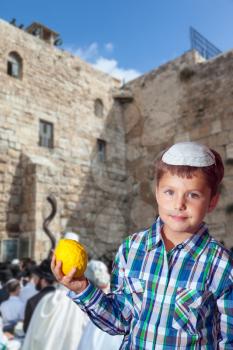 The greatest shrine of Judaism is the Western Wall of the Temple. Autumn Jewish holiday Sukkot. Beautiful Jewish boy with green eyes, in white skullcap, with etrog in his hand 