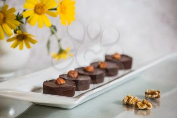 Portion small chocolate cakes are decorated with nuts. Gonfectionery desserts. Background -  white vase with field chamomiles. Professional bakery