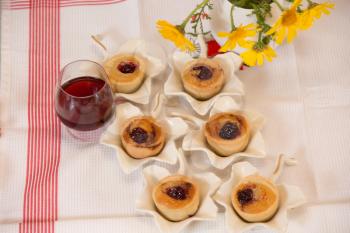  Professional baking. Magnificent portioned tartlet cakes with filling of mousse. Background - white porcelain elegant vases, a glass of red wine and wild flowers