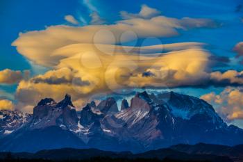 Snow-covered rocks of Los Cuernos. Magnificent orange clouds in the rays of the sunset. The concept of extreme and active tourism. Torres del Paine National Park