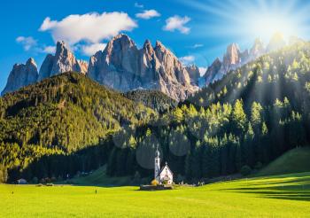 The concept of eco-tourism in Alpine meadows. The morning sun illuminates green valley and church of Santa Magdalena in the Dolomites