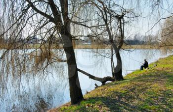 Royalty Free Photo of a Person Sitting on a Lakeshore by Trees in Spring