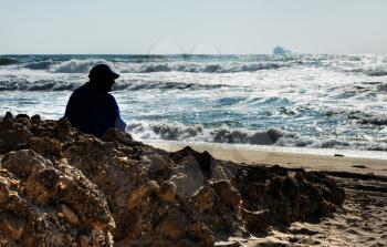Royalty Free Photo of a Man Sitting on Rocks at the Beach
