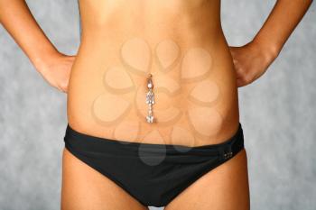 belly with piercing of the slim girl in black underwear on the gray background