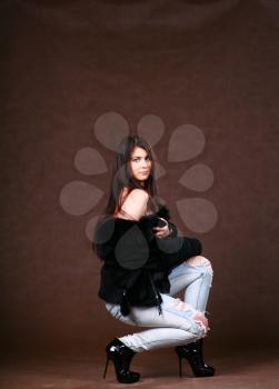 attracive young woman in a fur coat and jeans on browm background