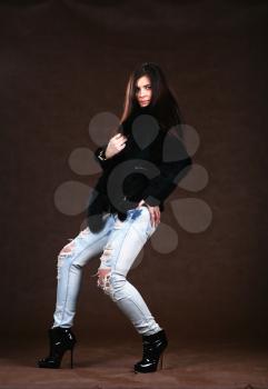 attracive young woman in a fur coat and jeans on brown background