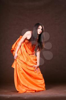 Attractive girl in orange fabric studio shot over brown background
