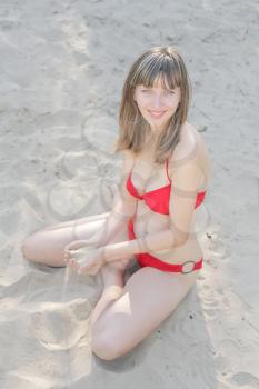 Beautiful girl sitting on the sand red bikini