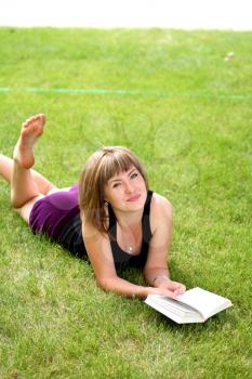 Young beautiful girl reading in the park laying on the grass