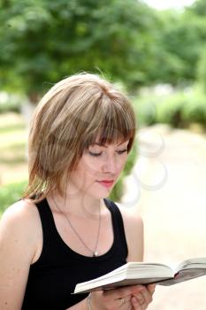 fun, young and charming woman with short hair, holding an open book, read against the background summer green park