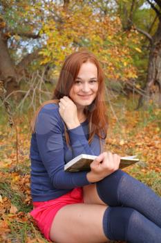 young, beautiful girl holding an open book, read background fall park