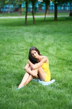 Portrait of a beautiful young woman with long brunette hair lying on the grass in a park