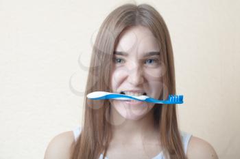 Dental Hygiene Funny Concept - A head and shoulders view of a blond woman with teeth brush in the mouth on the baige background