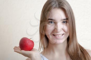 Beautiful blonde woman holding a red apple in right hand - health concept. Pretty smile deep blue eyes