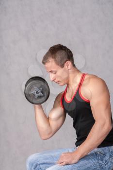 attractive athletic male torso with dumbbell sitting on gray background