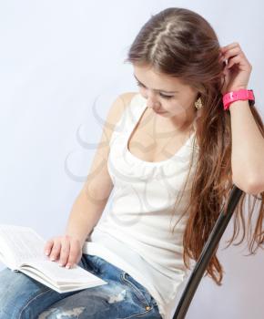Closeup portrait of a young smiling woman sitting on a chair in jeans reading a book