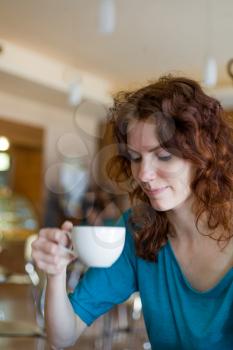Redhead women sitting in the cafee and holding cup of coffee in the hands looking away