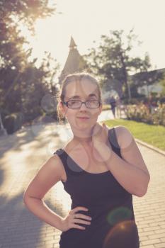 Cute romantic girl, attractive blond woman enjoying autumn yellow sunlight. She weared black tank top and glasses. Looking at camera with light smile. Back lit with lens flares.