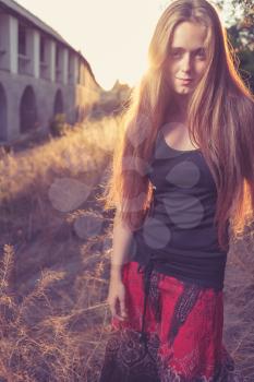 young blond women looking very seriously weared red skirt and black tank top.  Against gold sunset light. Autumn time. Backlit