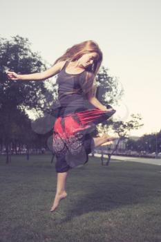 Long Haired Blonde  jumps on a green grass in evening time in city park . Girl jumping like flying bird.