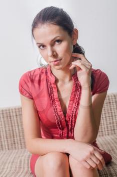 brunette looking at camera. 20s female weared red dress sitting on sofa indoors
