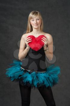 Ballet dancer weared tutu skirt with heart-shaped pillow in hands. Vertical shot of the beautiful young woman holding a heart shaped red pillow and smiling