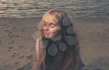 Pretty blond girl on a sandy sea shore relaxed with her eyes closed