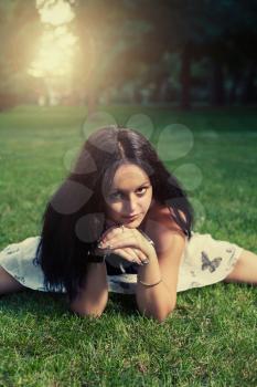 Brunette lying on green grass and looking at camera