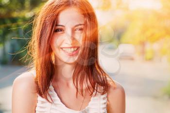 Smiling redhead outdoors backlit by sun , shot with flares.