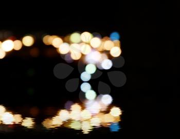 City lights in the background with blurring spots of  light reflected in water below