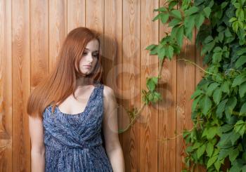 Long haired redhead women leaning against plank background with green leaves of ivy or grape over