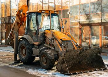 Bulldozer in the street in front of glass wall of modern building vintage color-look.