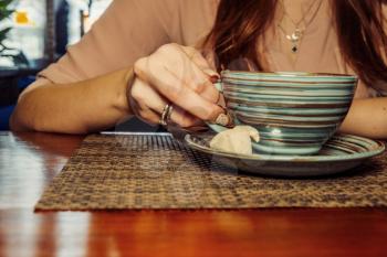 Cup of coffee on a wooden table, the girl holds her hand on one cup of coffee . A photo depicting a melancholic mood in loneliness, copyspace in foreground.