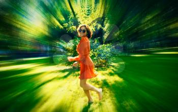 Defocused image of summertime fun. Young woman in red dress dancing on grass blurred shot.