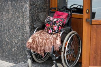 Wheelchair stands at the door of the state office in Russia. Black and red stroller with brown and white textile