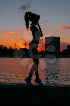 Happy sporty girl posing at sunset waterfront. Enjoy and breathe fresh air. Evening sports life outside.