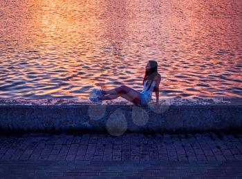 Daydreaming Girl sitting on pier and looking at the river side view sunset time