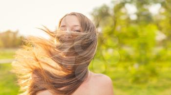 Happy lady face wrapped in her long blond hair by blow of the wind, joyness and freedome outside, warm summertime image.