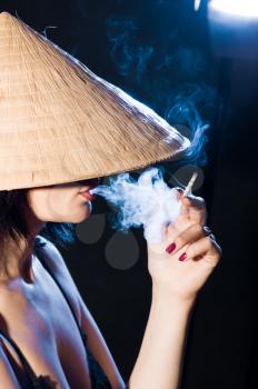 Royalty Free Photo of a Woman Smoking While Wearing a Vietnamese Hat 